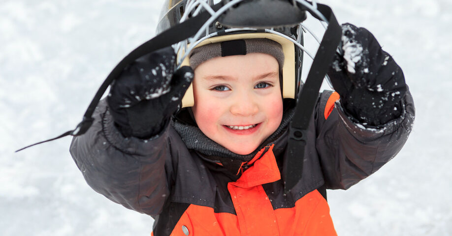 Lapsi nostaa jääkiekkokypärän visiiriä ja hymyilee kameralle