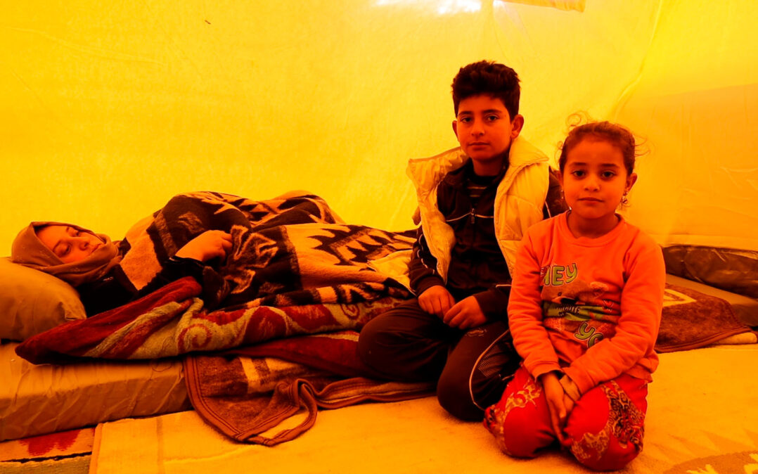 Kaksi lastaa istuu patjalla makaavan, maanjäristyksessä loukkaantuneen äitinsä vieressä.