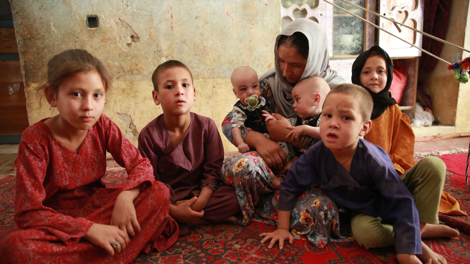 Äiti ja lapsia istumassa matolla kotonaan Afganistanissa