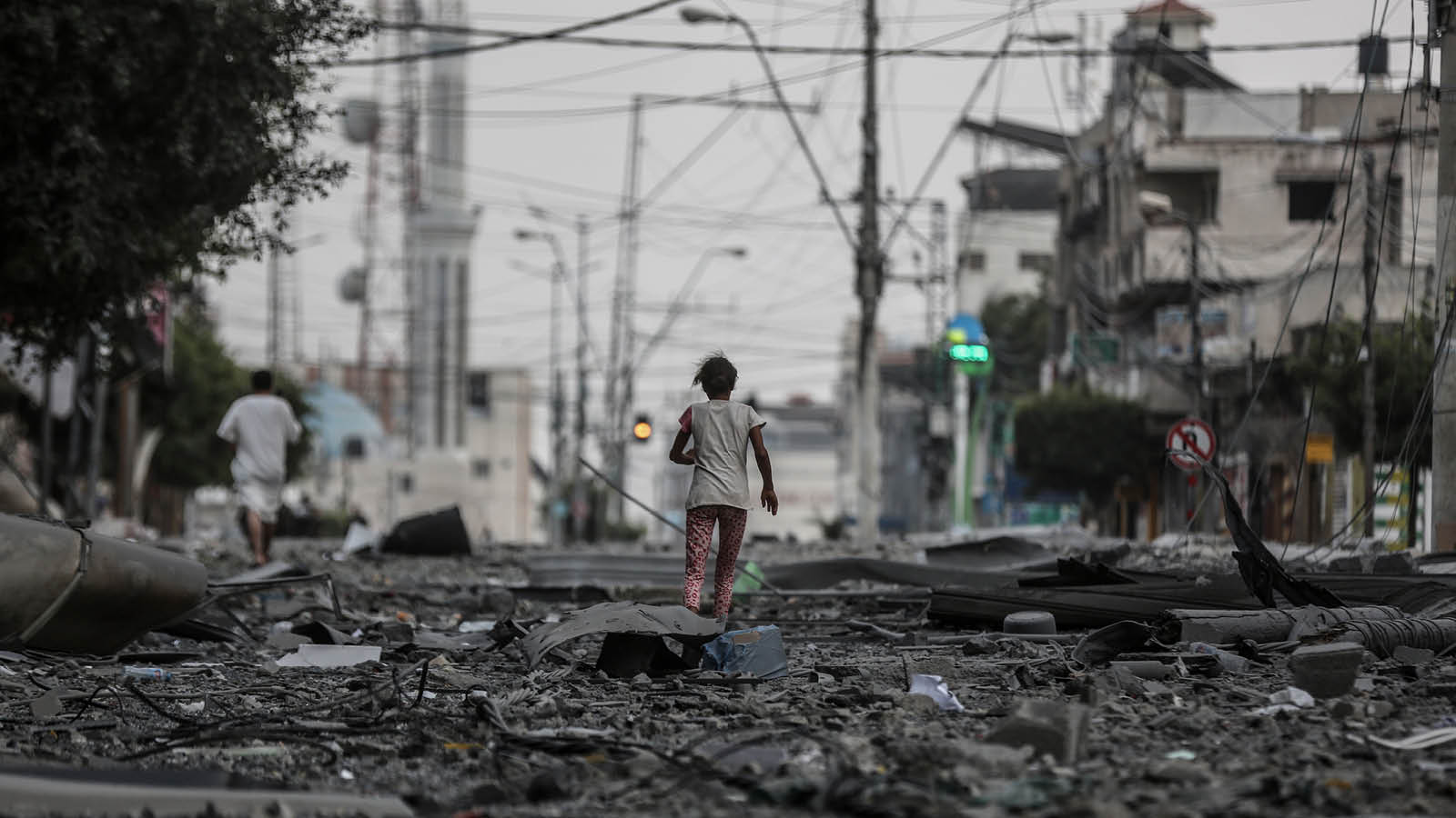 Lapsi juoksee ilmaiskuissa tuhoutuneessa Gazassa. Kadulla romua ja taustalla olevat rakennukset ovat tuhoutuneet.