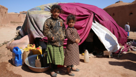 Kaksi pientä lasta lakanoista tehdyn teltan edustalla.