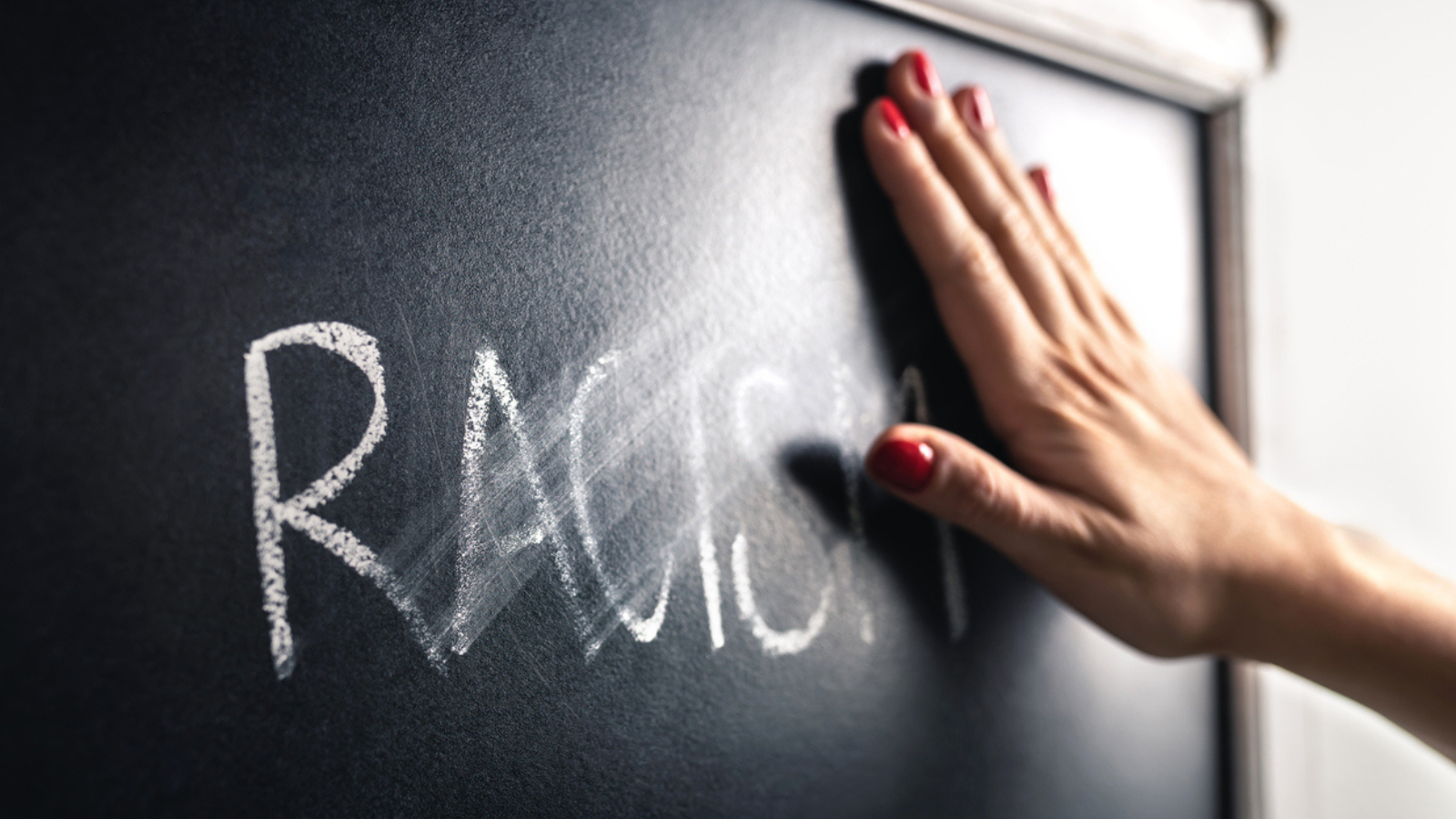 Kuvituskuva rasisminvastaiseen päivään. Kuvassa liitutaululla lukee englanniksi sana rasismi, ja näkyy sanaa pyyhkivä käsi.