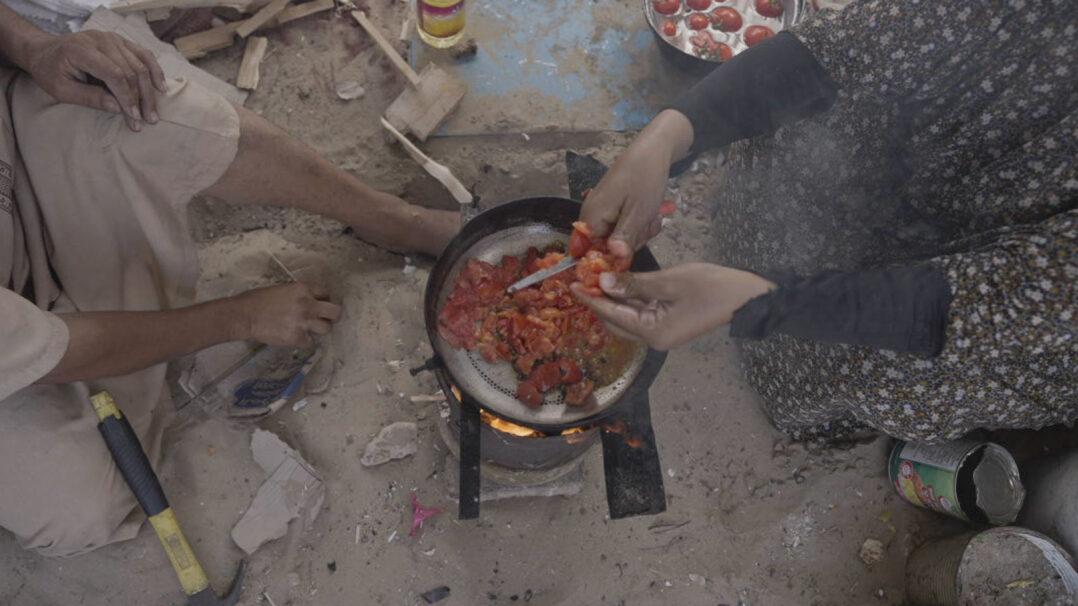 Ihminen pilkkoo tomaattia padan yllä Gazassa