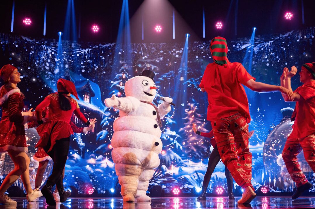 Kuvassa Masked Singer -hahmo Lumiukko laulaa jouluisella lavalla tanssijatonttujen ympäröimänä.